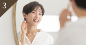 鏡の前で笑顔で身だしなみを整える女性の様子。