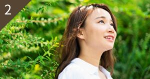 自然の中で空を見上げる笑顔の女性の様子。