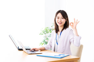 パソコンの前でOKサインをしながら笑顔を見せる女性の様子。